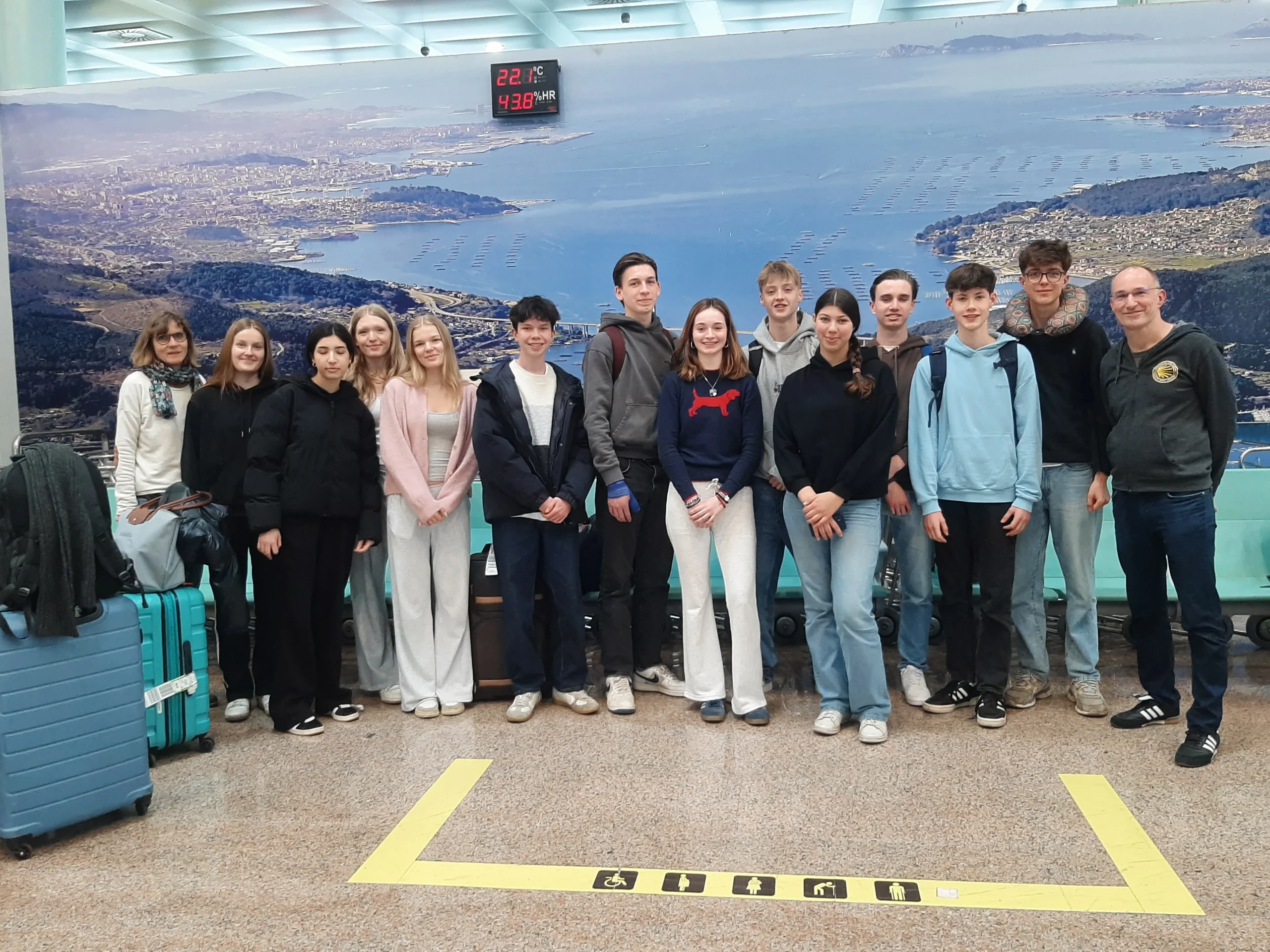 Schülergruppe steht vor großem Plakat am Flughafen